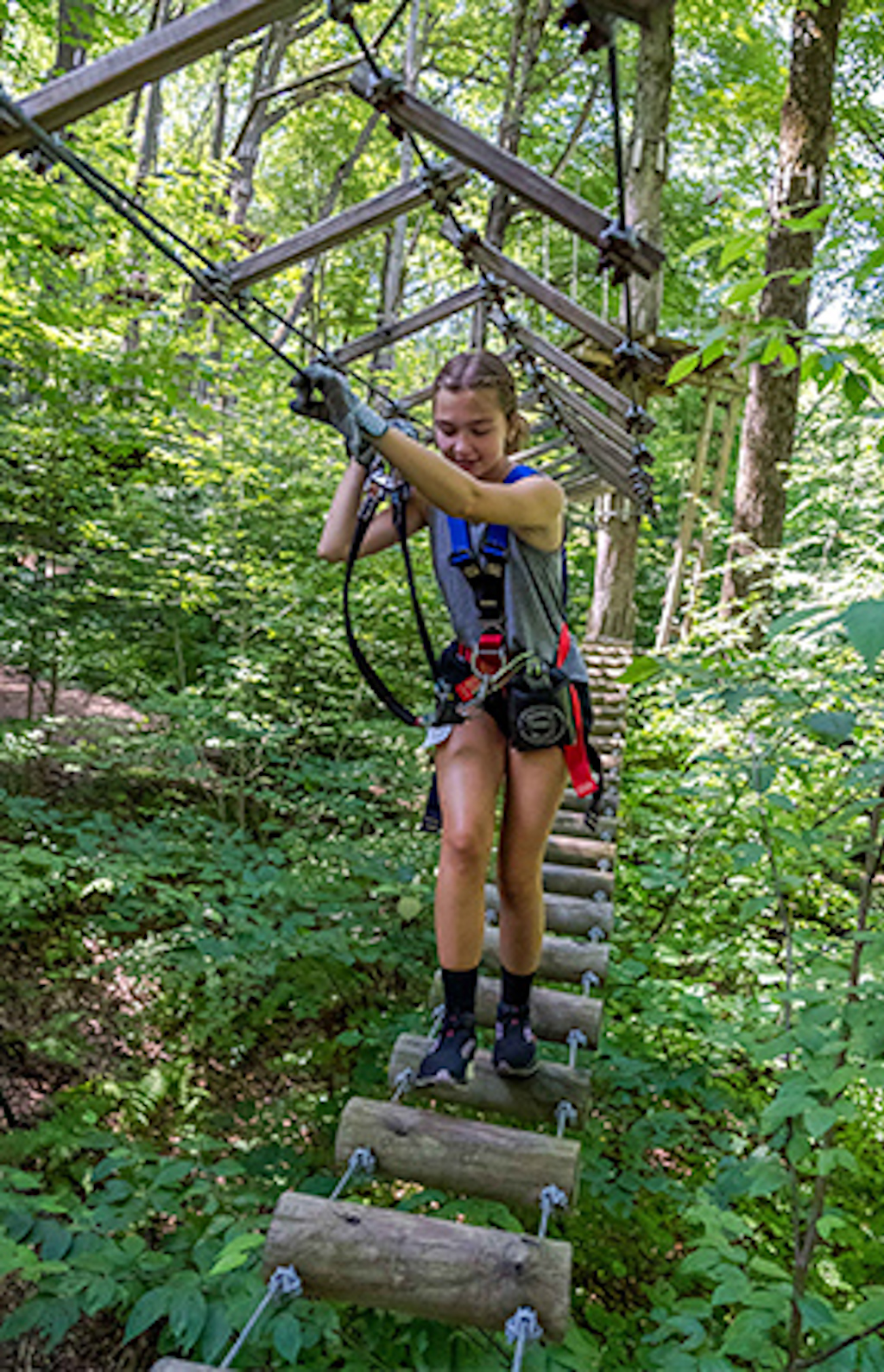 A young lady makes her way across a wooden bridge obstacle at Sky High Adventure Park.